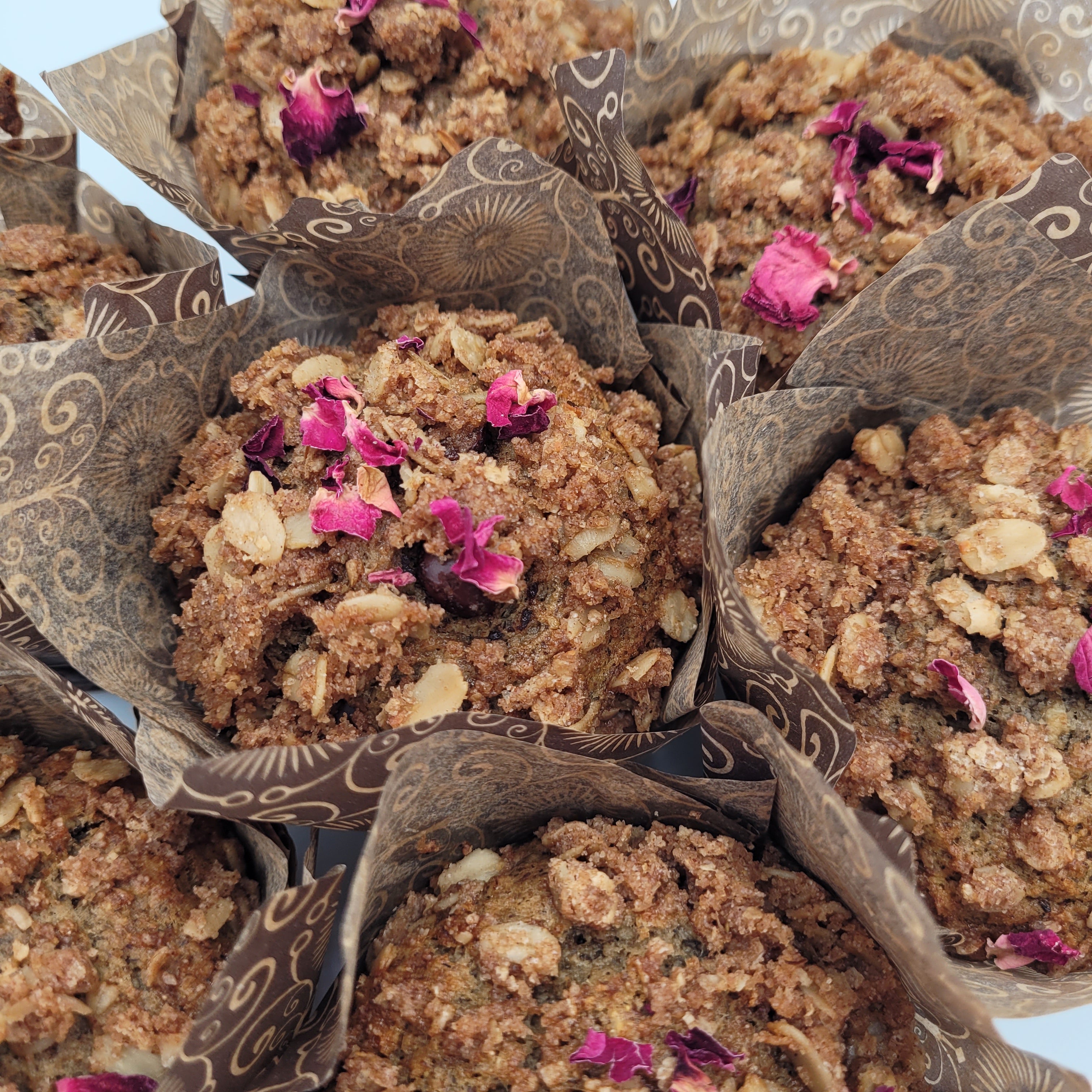 Muffins with pink rose petal toppings in decorative paper cups on a white background